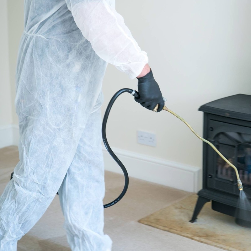 A pest controller carrying out flea fumigation in a home. They are wearing a white paper hazmat suit and black gloves.